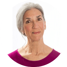 A woman with grey hair wearing a pink shirt.