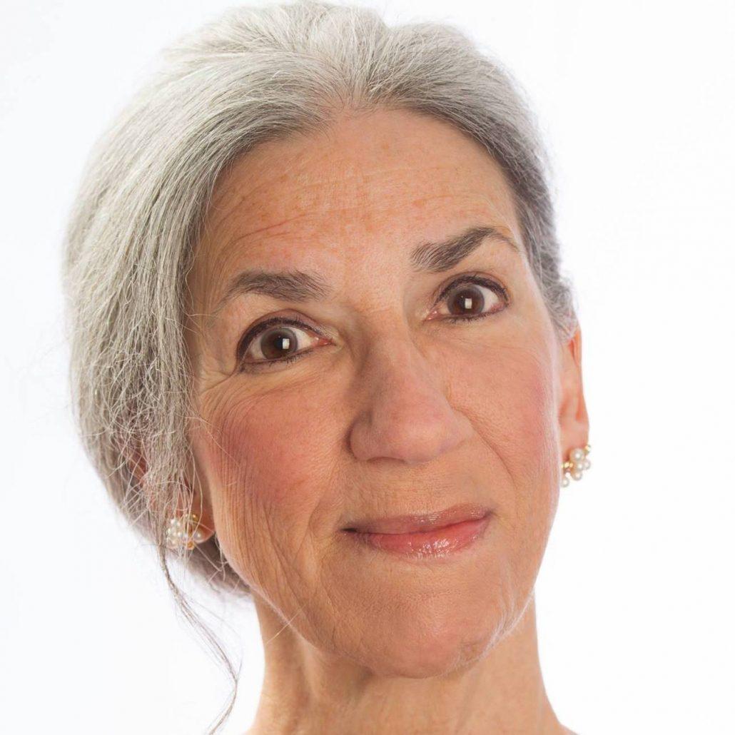 A woman with grey hair is smiling for the camera.
